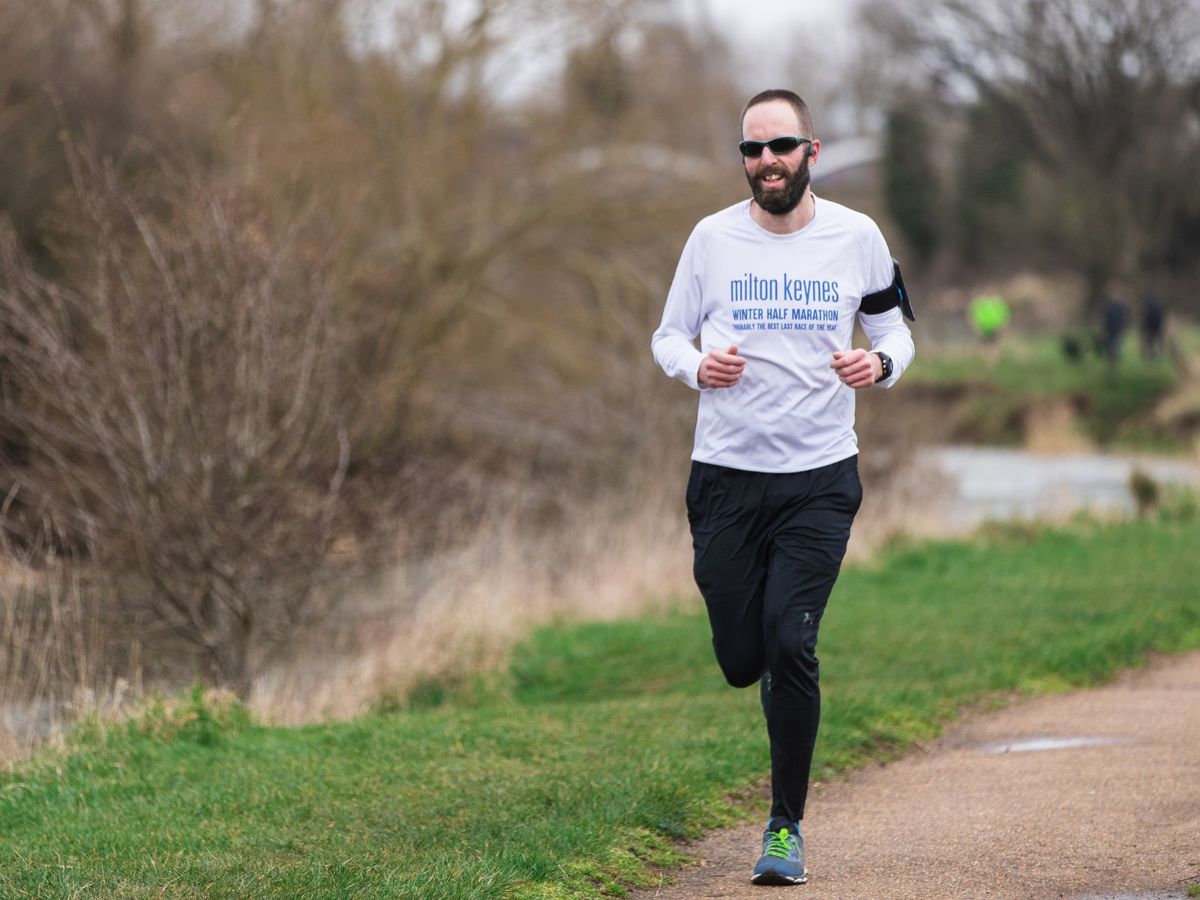 Person running along a river wearing MK Half Marathon T Shirt
