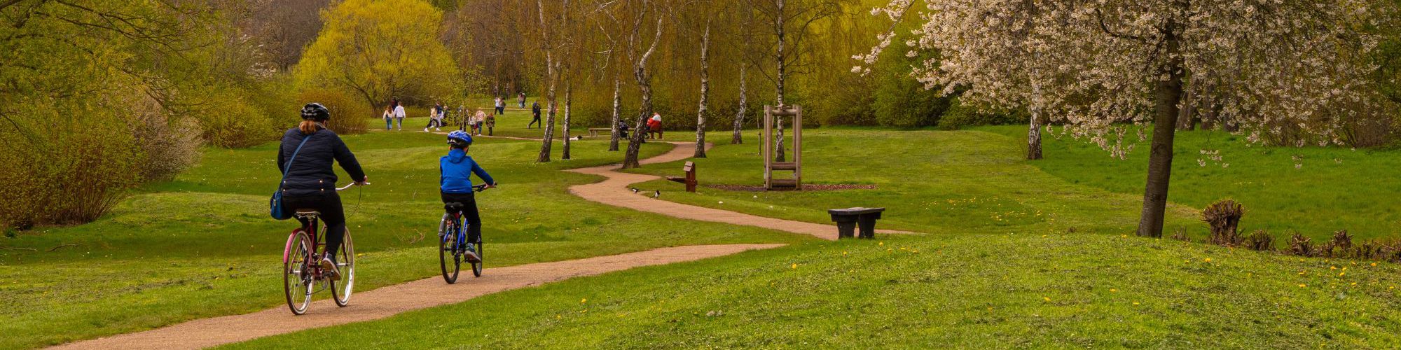 Two people cycling along pathway around Willen Lake with pedestrians in the distance