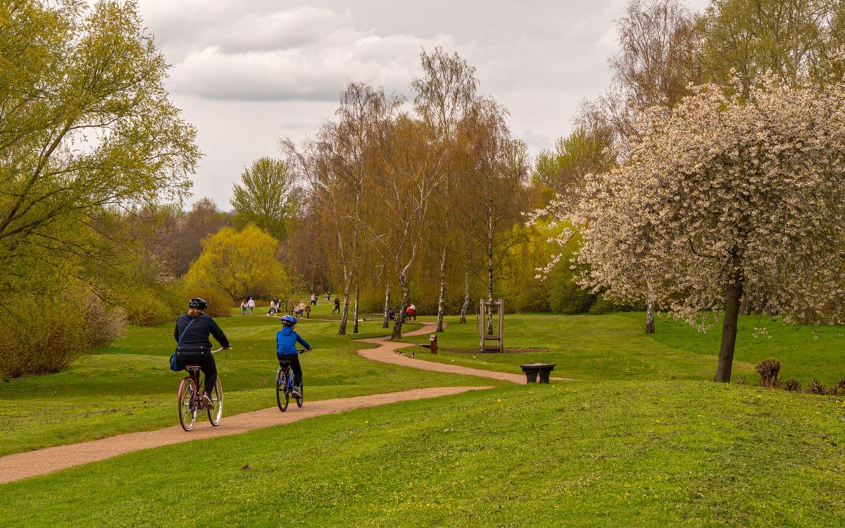 Two people cycling along pathway around Willen Lake with pedestrians in the distance