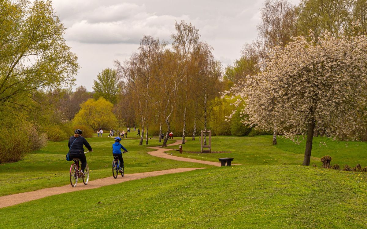 Two people cycling along pathway around Willen Lake with pedestrians in the distance