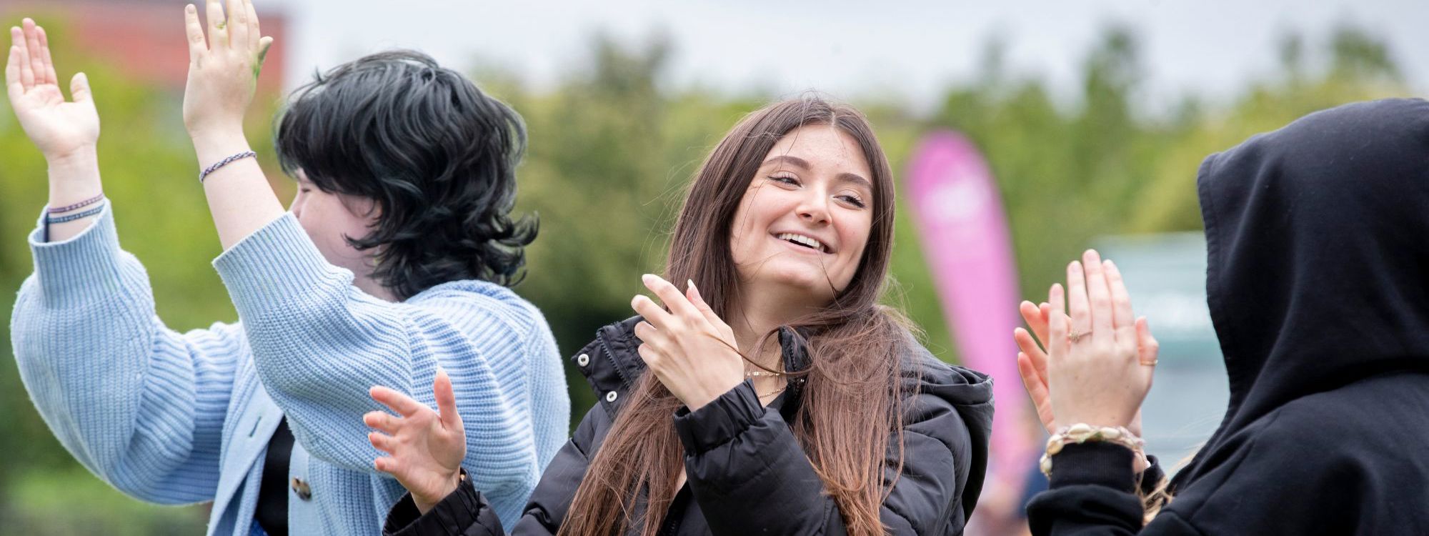three teenagers smiling and clapping at an event 