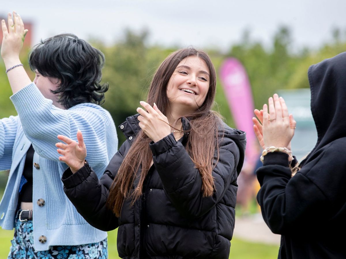 three teenagers smiling and clapping at an event 