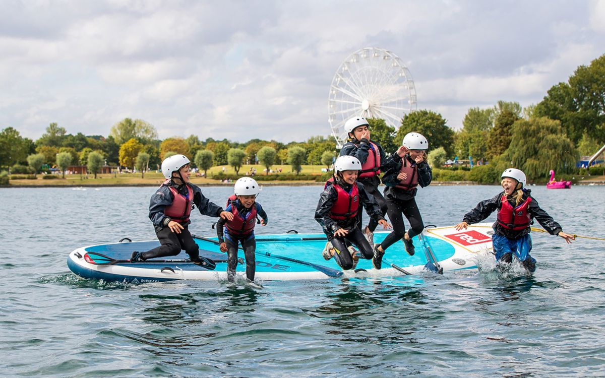 Group of children jumping off mega SUP board into Willen Lake