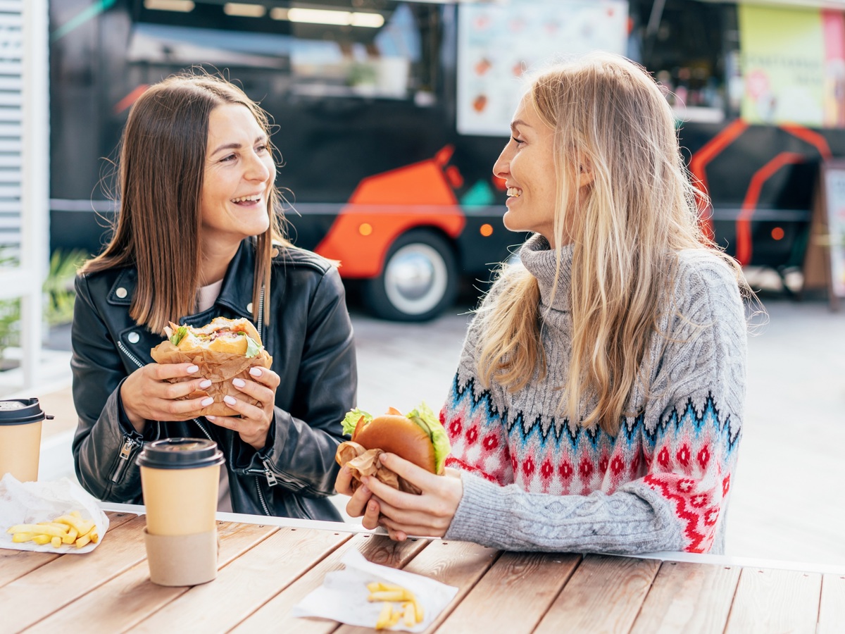 Two people sat at a table eating a burger at a street food event
