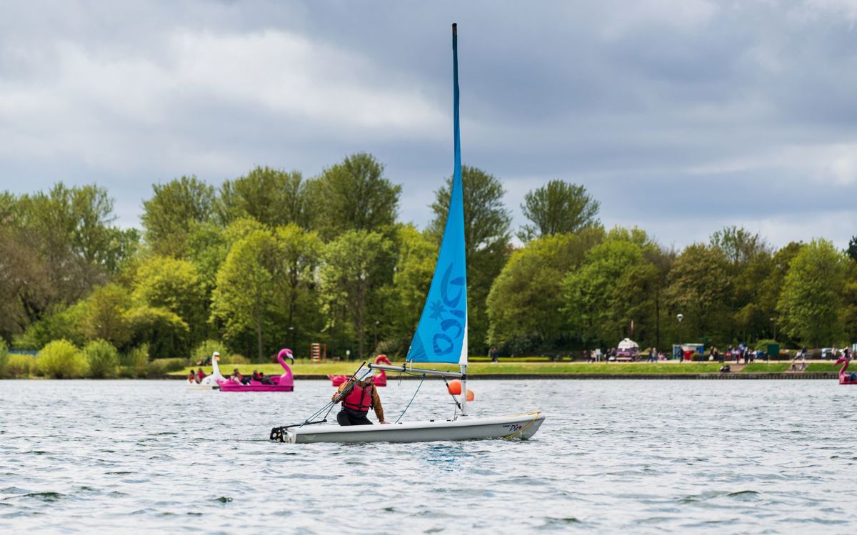 Person sailing on Willen Lake with pedalos in the background