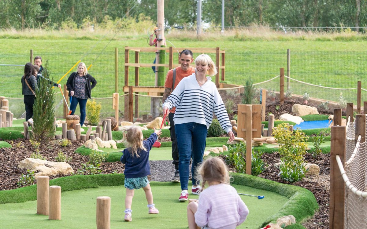 Parent passing golf club to child at Adventure Golf