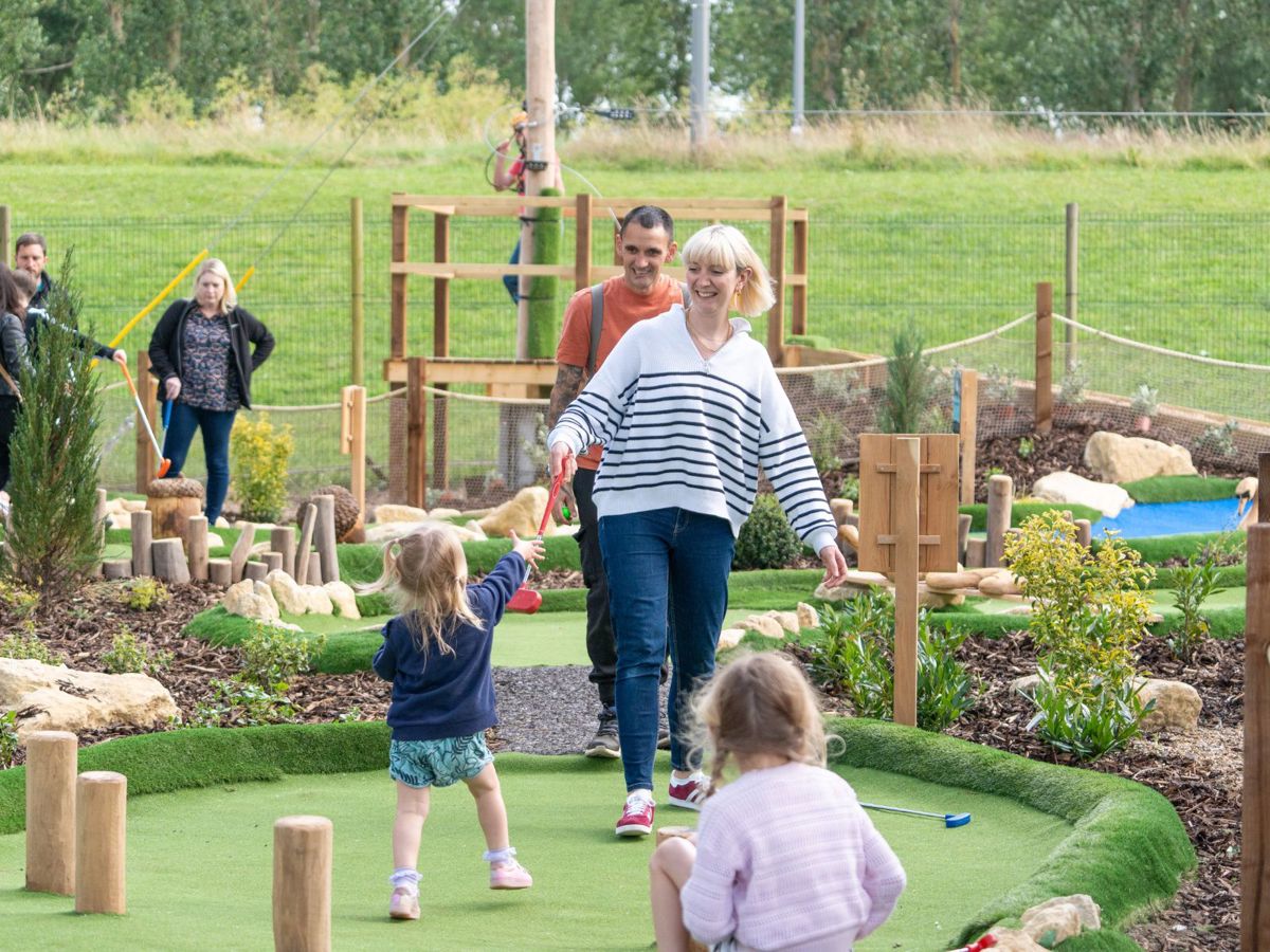 Parent passing golf club to child at Adventure Golf