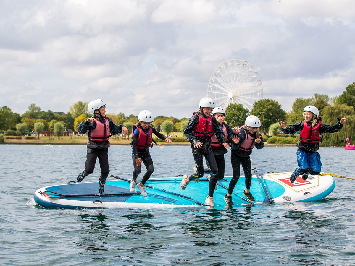 Group of children jumping off mega SUP board into Willen Lake
